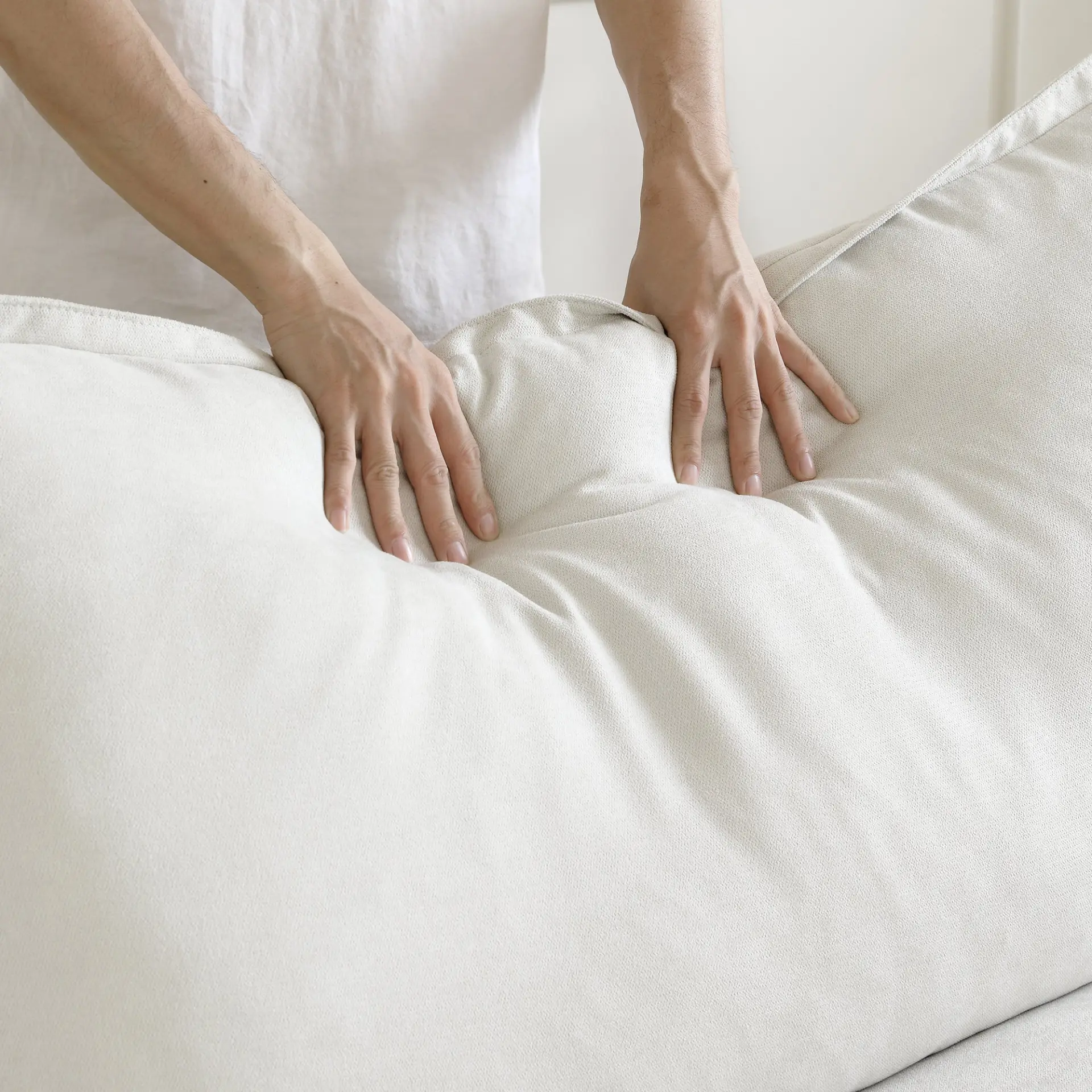 Hands adjusting a plush white Ascend cushion, showing the soft washable performance fabric